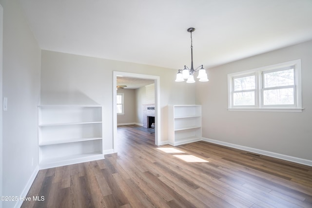 unfurnished dining area featuring wood-type flooring, a fireplace, and a notable chandelier