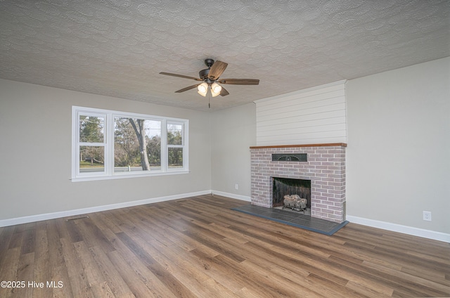 unfurnished living room featuring wood-type flooring, a brick fireplace, ceiling fan, and a textured ceiling