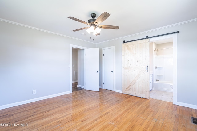 unfurnished bedroom with crown molding, ceiling fan, ensuite bathroom, a barn door, and light wood-type flooring