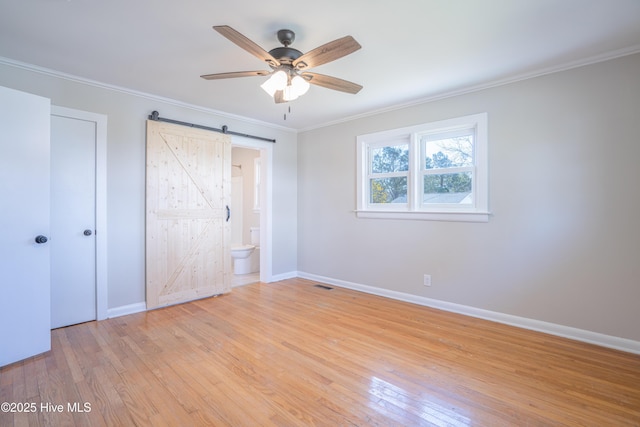 unfurnished bedroom with connected bathroom, ornamental molding, a barn door, and light wood-type flooring