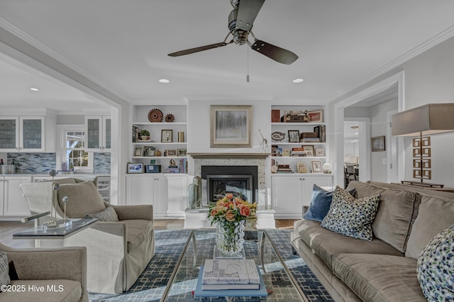 living area featuring built in features, a ceiling fan, crown molding, light wood-type flooring, and a fireplace