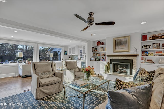 living area with built in shelves, wine cooler, a fireplace, ornamental molding, and wood finished floors