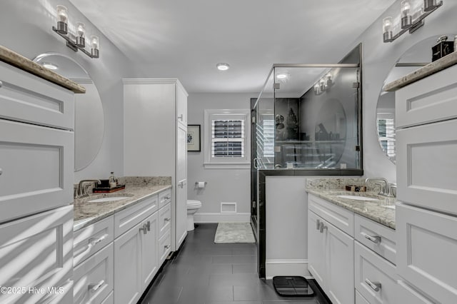 full bathroom featuring two vanities, a sink, a shower stall, and toilet