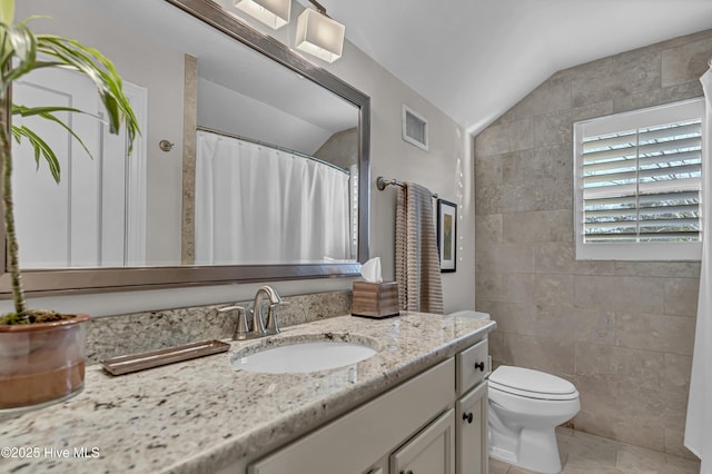 full bathroom with toilet, vanity, visible vents, vaulted ceiling, and tile walls