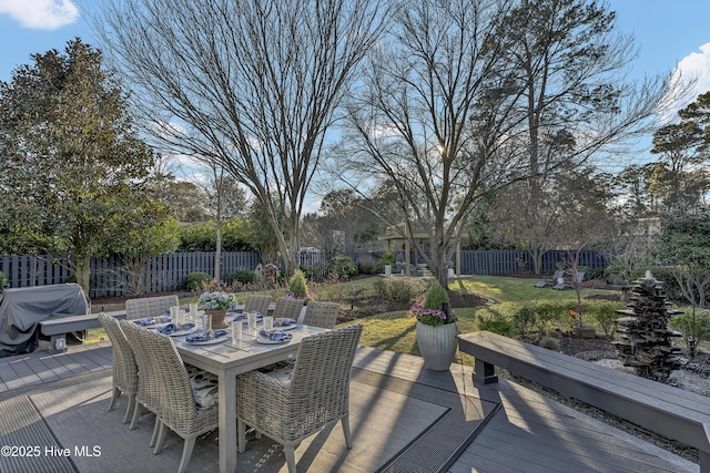 deck with outdoor dining space, a fenced backyard, and a lawn