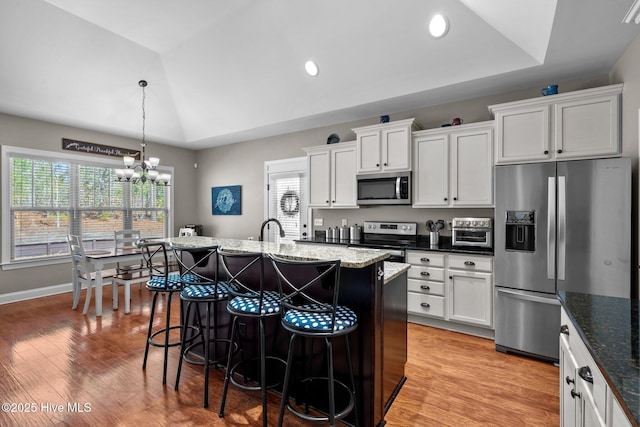 kitchen featuring a center island with sink, a raised ceiling, hanging light fixtures, appliances with stainless steel finishes, and white cabinetry