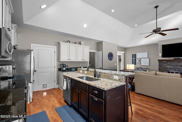 kitchen featuring stainless steel appliances, open floor plan, a sink, dark brown cabinetry, and a kitchen breakfast bar