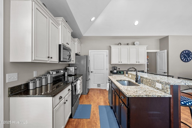 kitchen with stainless steel appliances, a sink, white cabinetry, light stone countertops, and an island with sink