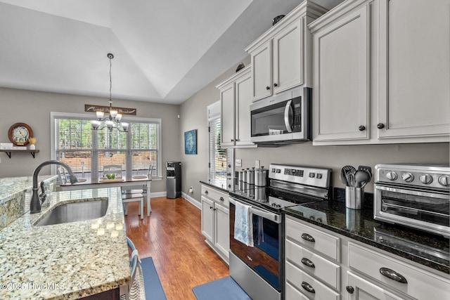 kitchen with white cabinets, light stone counters, appliances with stainless steel finishes, decorative light fixtures, and a sink