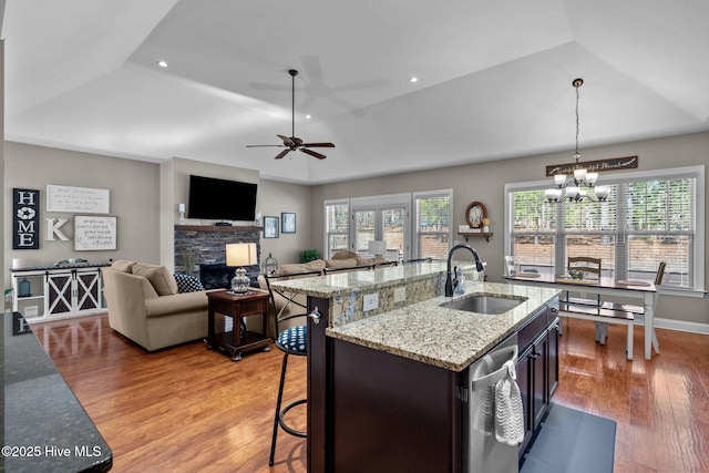 kitchen featuring a center island with sink, light stone counters, open floor plan, hanging light fixtures, and a sink