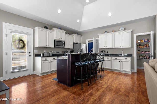 kitchen featuring a breakfast bar area, stainless steel appliances, white cabinets, vaulted ceiling, and a center island with sink