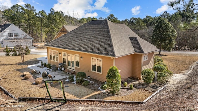 view of side of home featuring a shingled roof and a patio area