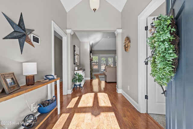 hallway with dark wood-style flooring, vaulted ceiling, and baseboards