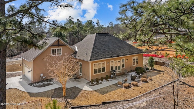 back of property with concrete driveway, roof with shingles, a patio area, and fence