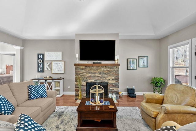 living area with a stone fireplace, wood finished floors, and baseboards