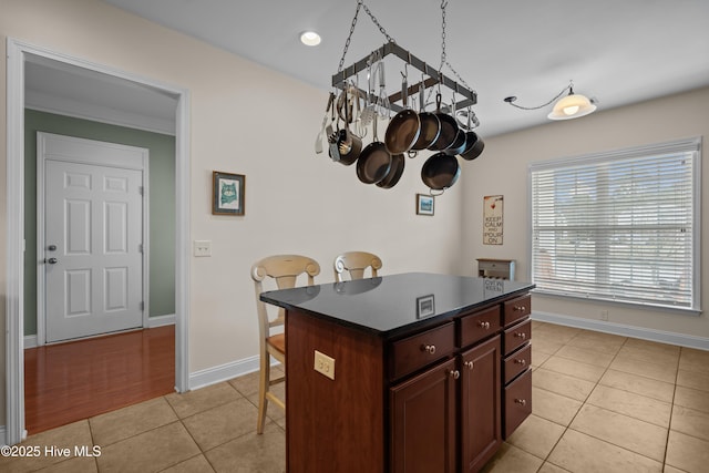 kitchen with a center island, a breakfast bar area, dark countertops, light tile patterned flooring, and baseboards