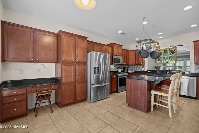 kitchen with a breakfast bar area, appliances with stainless steel finishes, backsplash, built in study area, and a center island