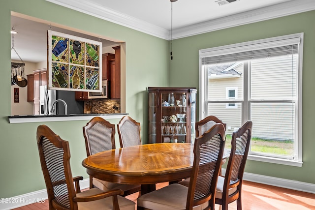 dining space with baseboards, light wood-style flooring, visible vents, and crown molding