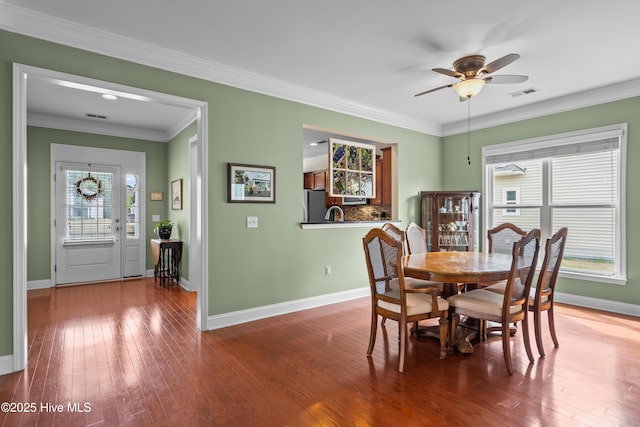 dining room featuring wood-type flooring, visible vents, crown molding, and baseboards