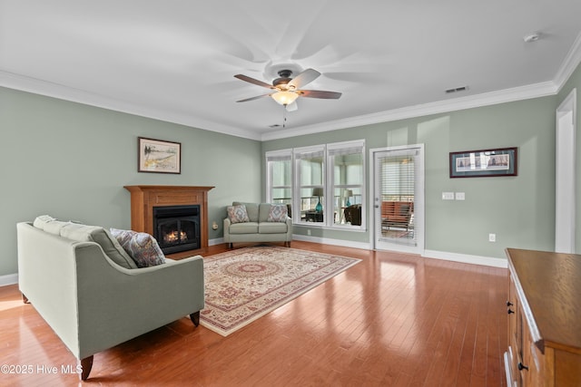 living area featuring a warm lit fireplace, ceiling fan, light wood-style flooring, visible vents, and crown molding