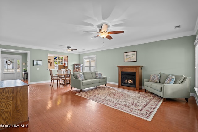 living room with a warm lit fireplace, hardwood / wood-style flooring, visible vents, baseboards, and crown molding