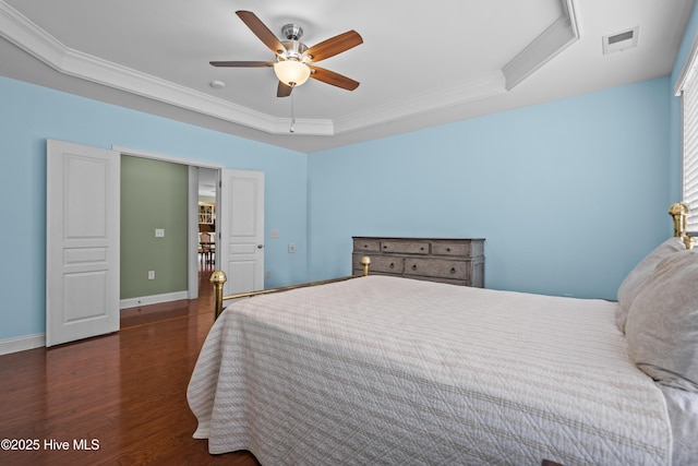 bedroom featuring a tray ceiling, crown molding, visible vents, wood finished floors, and baseboards