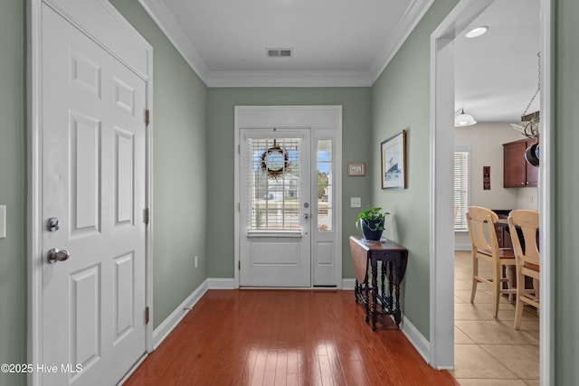 foyer entrance featuring light wood-style flooring, visible vents, baseboards, and ornamental molding