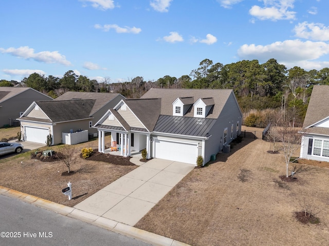 view of front facade featuring metal roof, an attached garage, covered porch, concrete driveway, and a standing seam roof