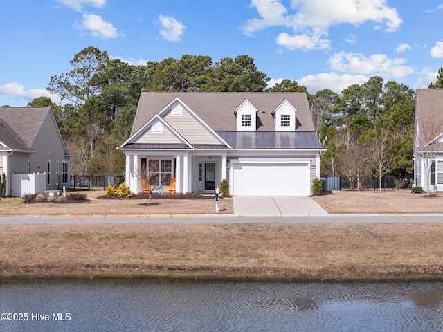 view of front facade featuring a water view, a standing seam roof, metal roof, fence, and driveway