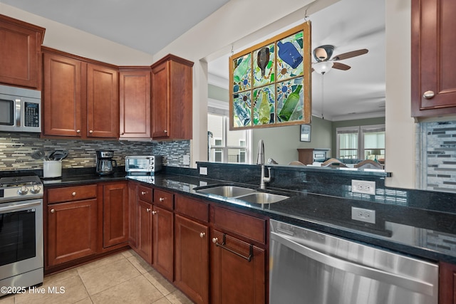 kitchen with backsplash, appliances with stainless steel finishes, light tile patterned flooring, a sink, and dark stone counters