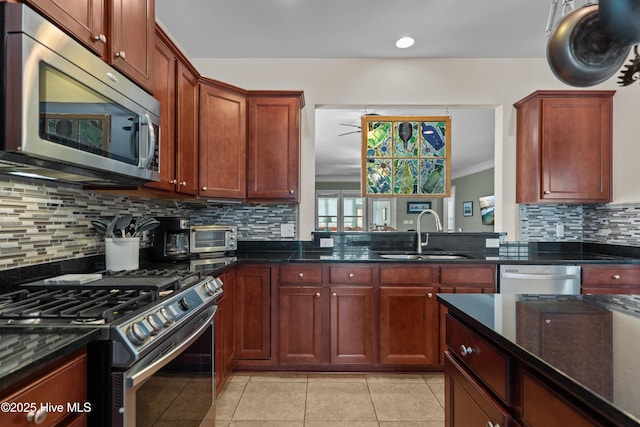 kitchen with light tile patterned floors, stainless steel appliances, a sink, backsplash, and dark stone counters