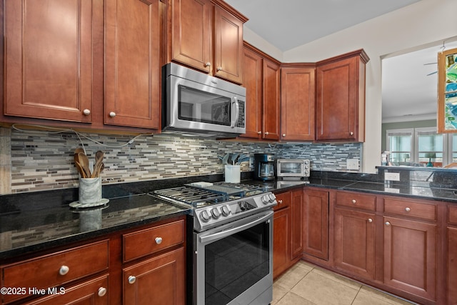 kitchen with light tile patterned floors, dark stone countertops, appliances with stainless steel finishes, and backsplash