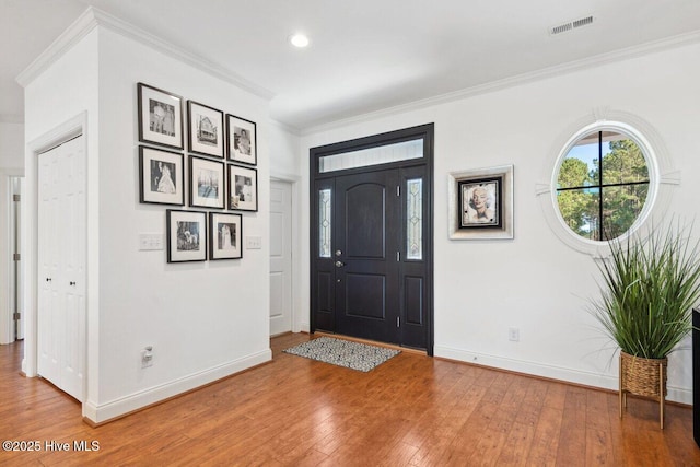 entryway featuring visible vents, baseboards, light wood-style floors, and ornamental molding