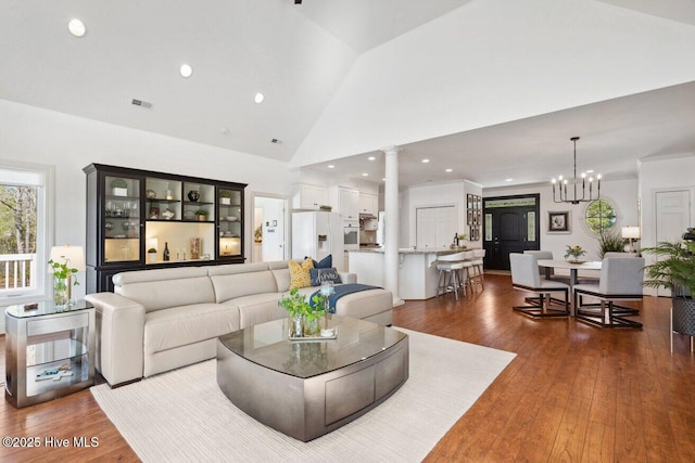 living area featuring visible vents, high vaulted ceiling, ornate columns, and wood-type flooring