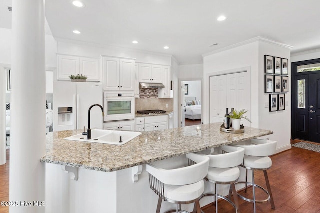 kitchen featuring a sink, backsplash, dark wood finished floors, white appliances, and white cabinets