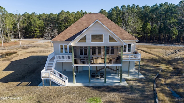 back of property with stairs, a patio area, a wooded view, and a shingled roof