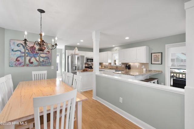 dining room featuring a notable chandelier, decorative columns, light wood-style flooring, and recessed lighting