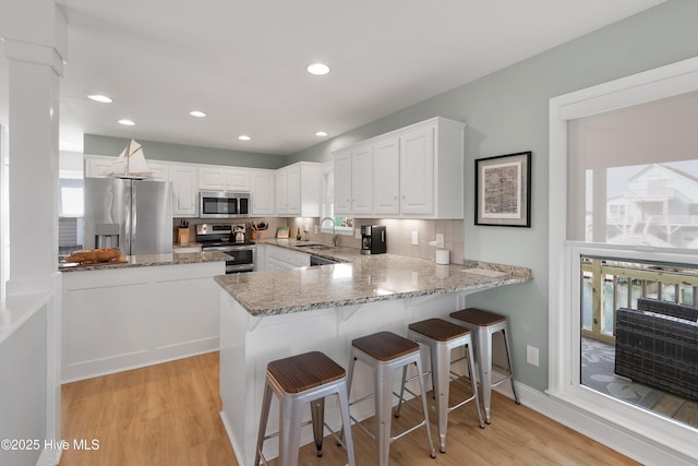 kitchen with appliances with stainless steel finishes, white cabinets, a sink, and a peninsula