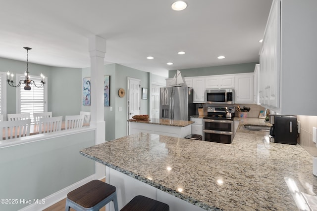 kitchen with a center island, stainless steel appliances, white cabinets, light stone countertops, and a peninsula