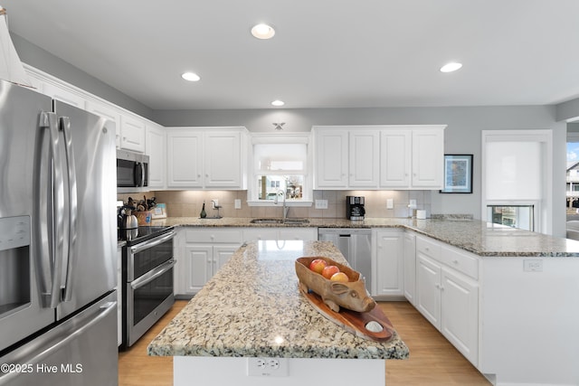 kitchen with appliances with stainless steel finishes, a peninsula, light wood-type flooring, white cabinetry, and a sink