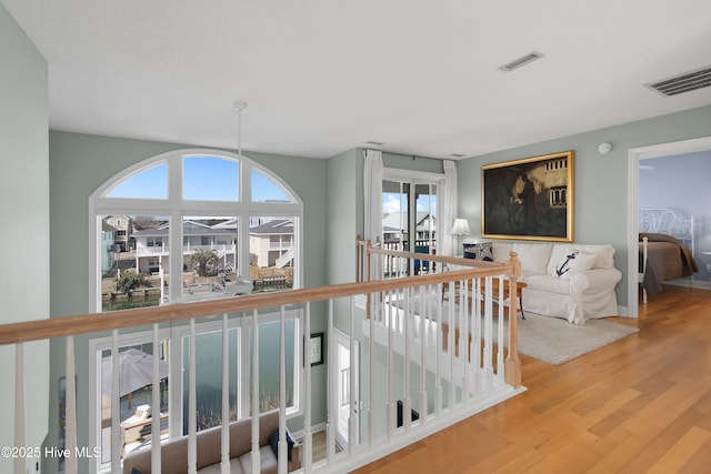 hall with an upstairs landing, wood finished floors, and visible vents