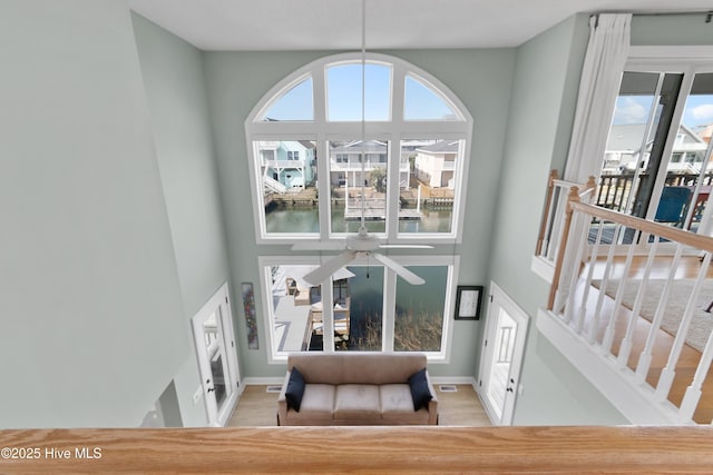 interior space with a water view, wood finished floors, a ceiling fan, and baseboards