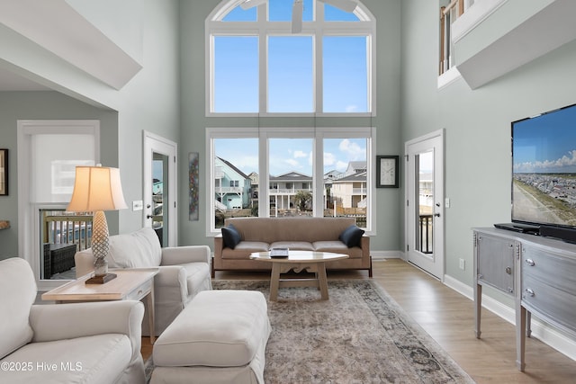 living area featuring a healthy amount of sunlight, light wood-style flooring, a towering ceiling, and baseboards