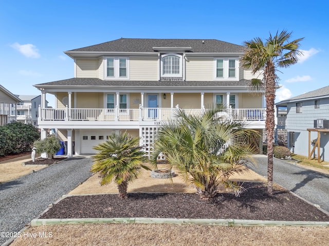 beach home featuring covered porch, driveway, roof with shingles, and a garage