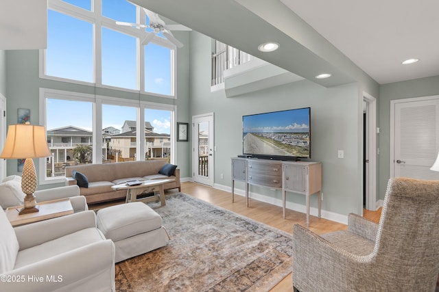 living area with baseboards, a ceiling fan, a towering ceiling, wood finished floors, and recessed lighting