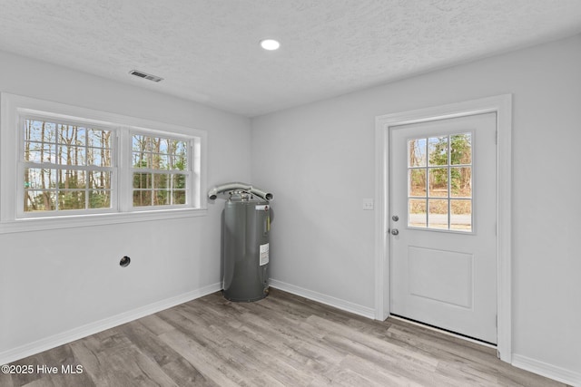 clothes washing area featuring a healthy amount of sunlight, light hardwood / wood-style floors, and a textured ceiling