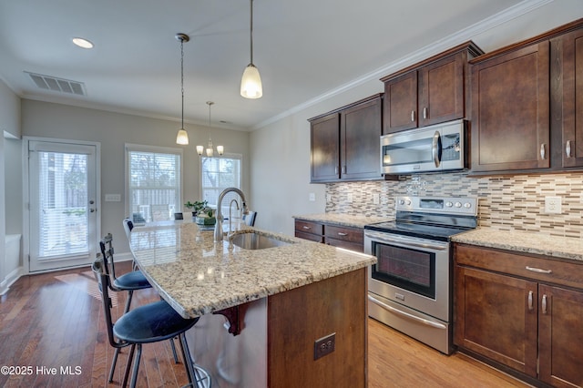 kitchen with sink, a breakfast bar, appliances with stainless steel finishes, a kitchen island with sink, and light stone counters