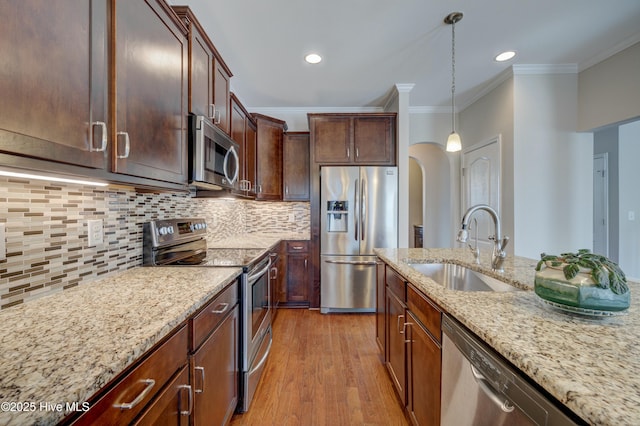 kitchen featuring pendant lighting, sink, stainless steel appliances, light stone counters, and ornamental molding