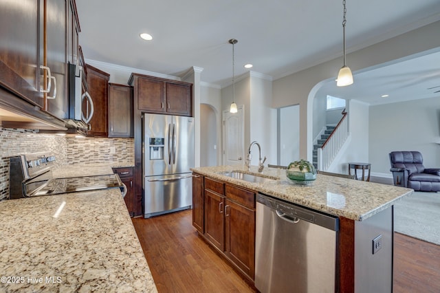 kitchen featuring pendant lighting, sink, appliances with stainless steel finishes, light stone countertops, and a center island with sink