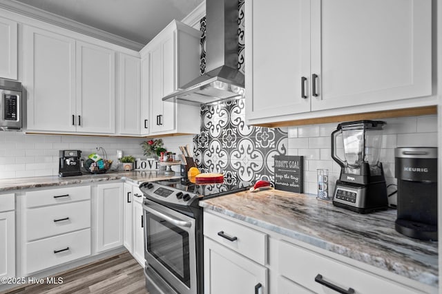 kitchen featuring white cabinetry, light stone counters, appliances with stainless steel finishes, wall chimney range hood, and backsplash